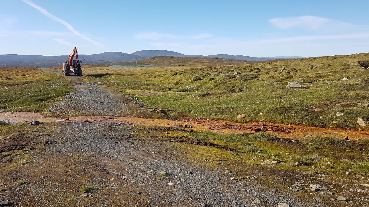 Gravemaskin på grusvei i fjellområde