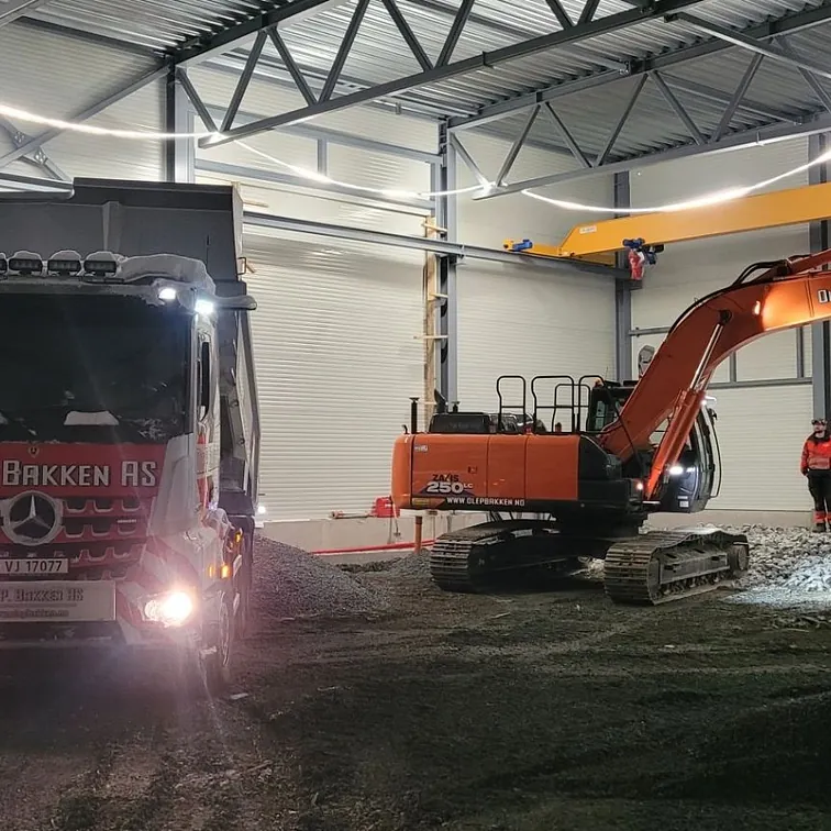 Gravemaskin og lastebil i hall